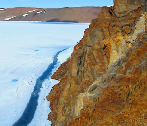 Expeditioners in background sampling rock with large cliff in foreground