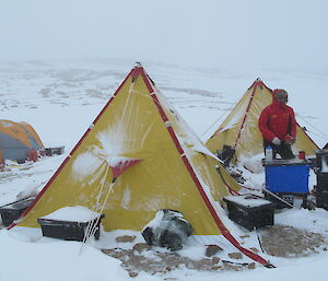 Expeditioners cook beside a polar pyramid tent during a storm