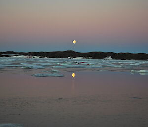 Moon reflecting on sea ice with land in background