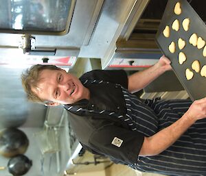 Chef smiling in the Davis kitchen while extracting a tray of heart shaped shortbread biscuits