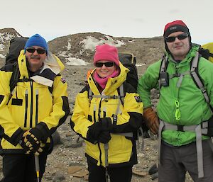 Three expeditioners smiling at the camera with background of rocky landscape