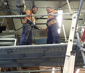 Two tradesmen on scaffolding looking down smiling at camera