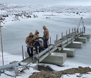 Three tradesmen hauling pipes on a steel walkway