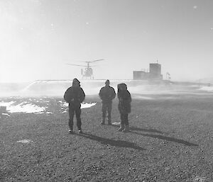 three expeditioners take cover as a helicopter lands