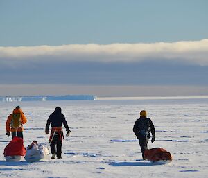 Three expeditioners hiking on an icy plateau dragging sleds