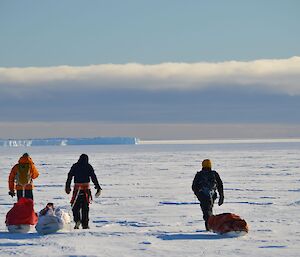 Three expeditioners hiking on an icy plateau dragging sleds