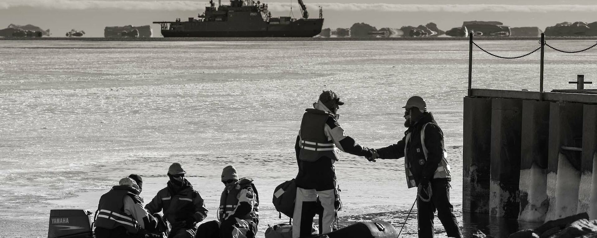 Expeditioners shake hands in foreground with resupply ship in background