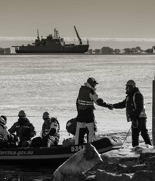 Expeditioners shake hands in foreground with resupply ship in background