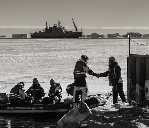 Expeditioners shake hands in foreground with resupply ship in background