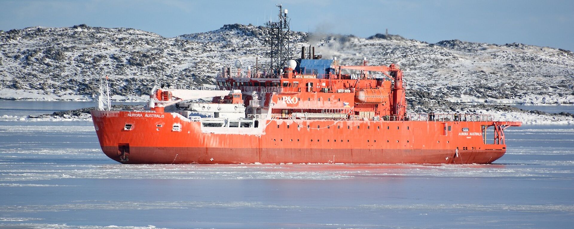 Large orange ice breaker ship in foreground. snow covered island in rear