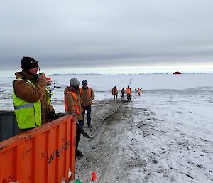 Expeditioner on radio to ship in foreground. others in background wave at ship in distance