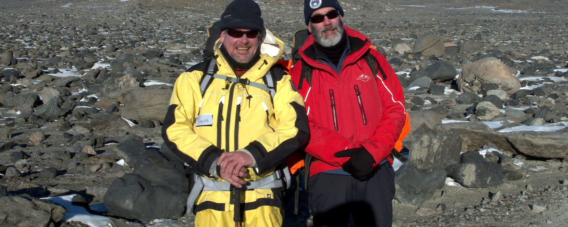 Two expeditioners, rocky terrain in background pose for photograph