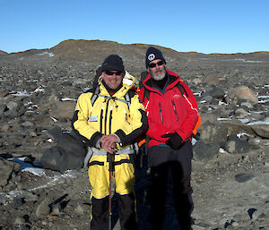 Two expeditioners, rocky terrain in background pose for photograph