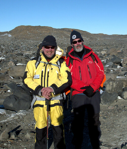Two expeditioners, rocky terrain in background pose for photograph