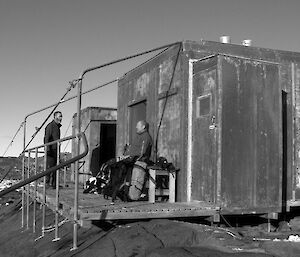 Two expeditioners stand on the balcony of a field hut