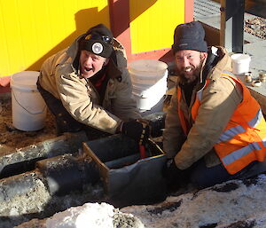 Two expeditioners facing camera whilst working on pipe work