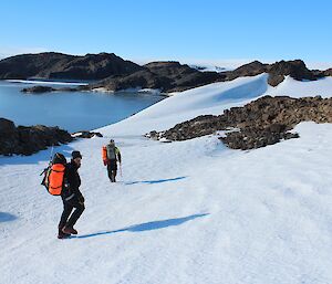 Two expeditioners hiking with rocky terrain in their background