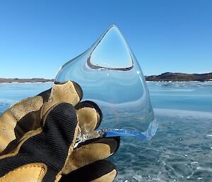Photo of triangular piece of ice reflecting image of background scenery