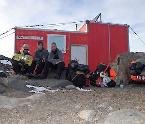 Three expeditioners pose in front of field hut