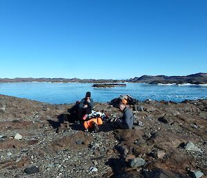 Two expeditioners eating lunch in foreground. Lake in background