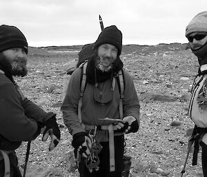 Three expeditioners posing in front of camera against rocky terrain