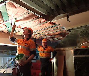 Expeditioner applying glue to a ceiling framework. another expeditioner stands in the background