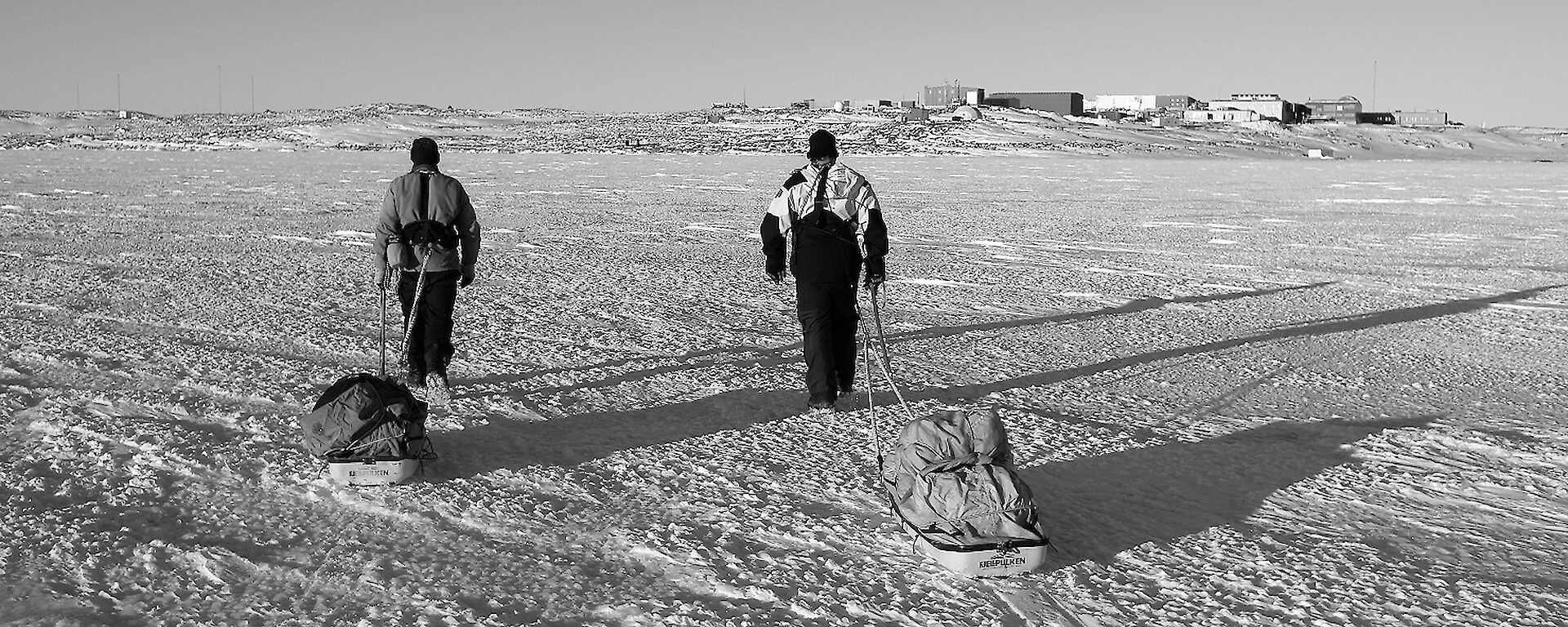 Two expeditioners man haul equipment across the sea ice towards station