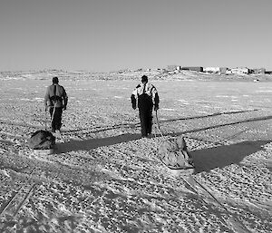 Two expeditioners man haul equipment across the sea ice towards station