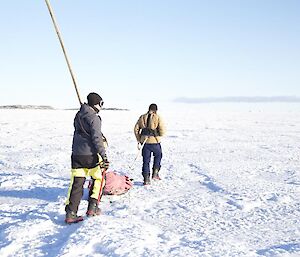 Two expeditioners walking on sea ice carrying sleds and bamboo poles