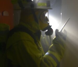 Expeditioner in fire fighting outfit talking on a radio in a darkened hallway
