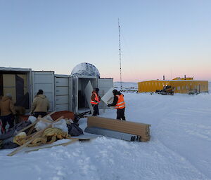 expeditioners unloading containers as a bobcat clears snow from the roads around station