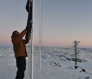 Expeditioner lowering the national flag with a snowy landscape in background