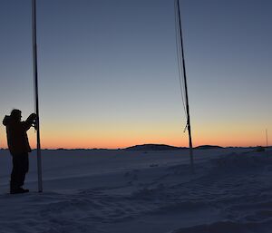 Expeditioner silhouetted against sunset behind icebergs