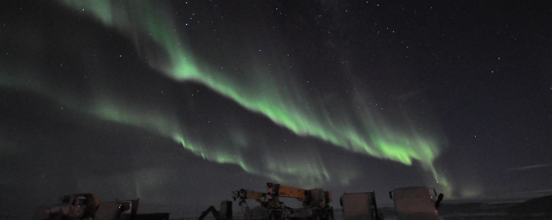Green Aurora australis above winterised vehicles on the Davis helipad