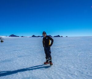 Expeditioner facing camera standing on ice with hills a backdrop