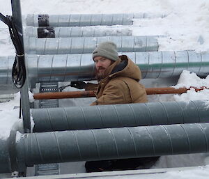 Expeditioner huddled beside a row of pipes