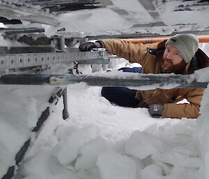 Expeditioner lying in a snow cavity beside a set of pipes carrying site services