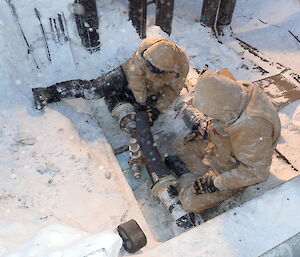 Expeditioners beside exposed pipe during snowfall installing insulation