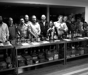 Expeditioners stand behind an extended table with 24 whisky bottles in front.
