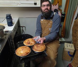 Expeditioner in a field hut taking pies out of the oven