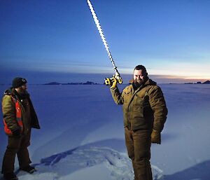 Two expeditioners facing camera one holding a sea ice drill