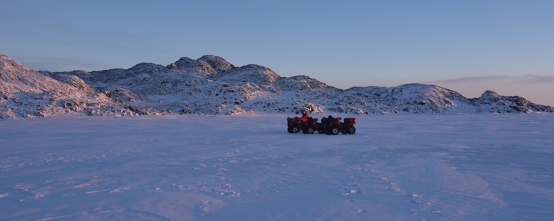 Quads in foreground on sea ice with islands covered in snow in the background