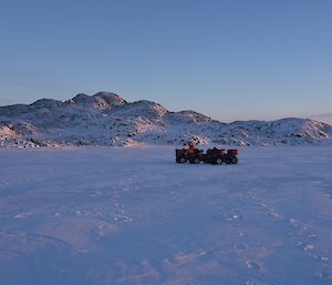 Quads in foreground on sea ice with islands covered in snow in the background