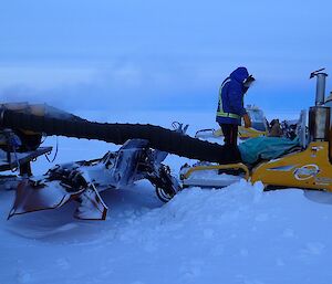 Expeditioner standing above a snow groomer as a heater with an extension tube defrosts the engine bay