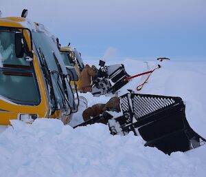 Two snow groomers being dug out of snowdrift by three expeditioners