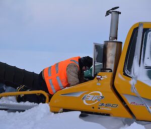 Expeditioner crouched over the engine of a snow groomer as it is being defrosted