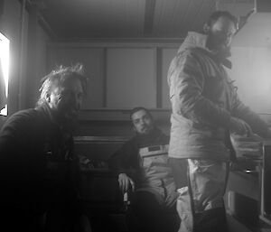 Three expeditioners facing camera inside a hut on the site during a break