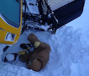 Expeditioner shovelling snow out from underneath a groomer