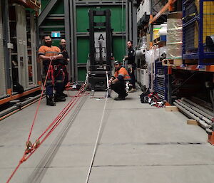 Four expeditioners facing camera inside a green supply warehouse with ropes practising technical search and rescue skills