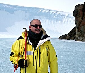 Expeditioner facing camera holding ice axe with glacier in background